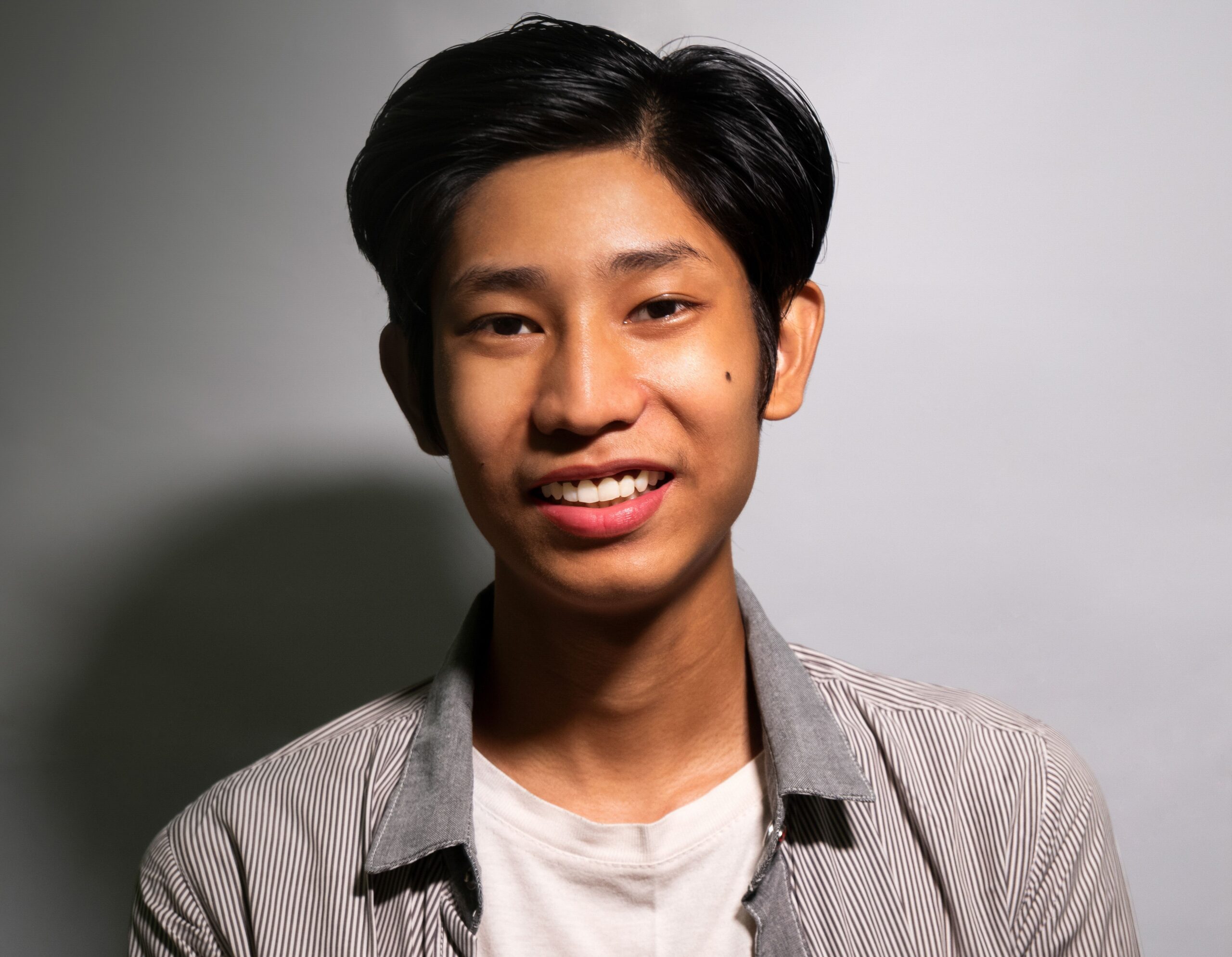 Close-up portrait of a smiling young man against a plain background in a studio setting.